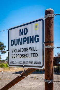 Close-up of a 'No Dumping' sign on a barbed wire fence emphasizing legal warning.